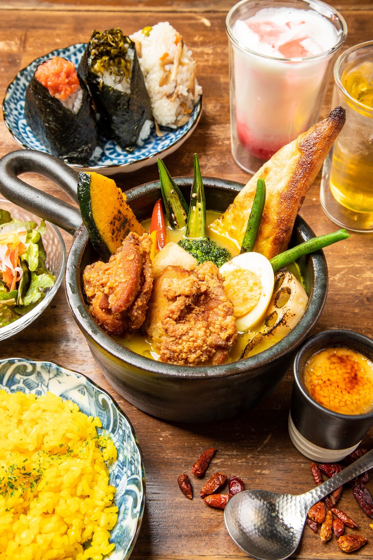 土鍋に入ったチキンのスープカレー。ゆで卵やかぼちゃ、オクラが彩り豊かで、ターメリックライス、おにぎり、サラダ、ドリンクが並んでいます。